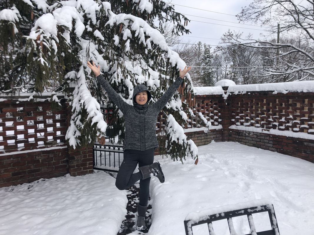 Motoko standing joyfully with arms raised in front of a snow-covered pine