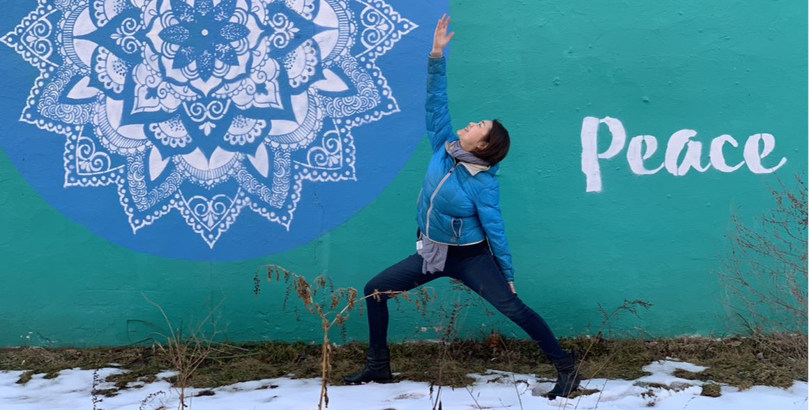 Motoko practicing yoga outdoors in front of a peace mural